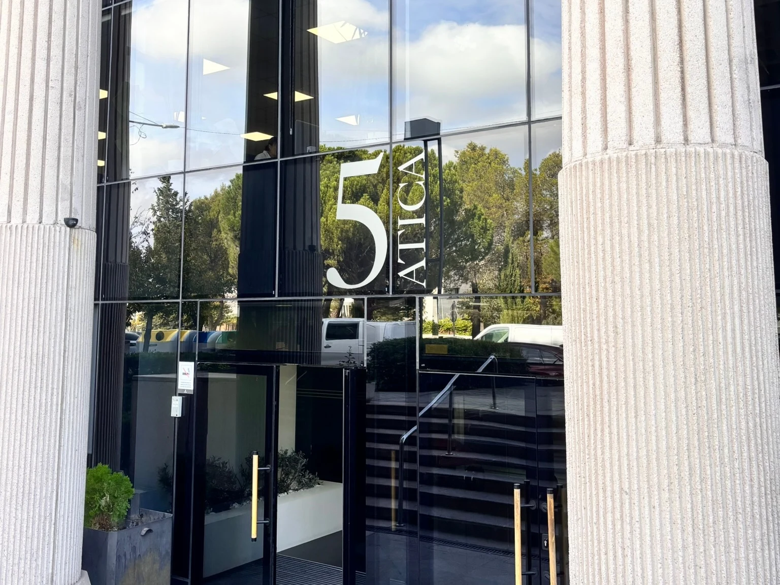 Entrada del Edificio Ática 5, con el rótulo 5 Ática sobre las puertas de cristal, entre dos columnas blancas